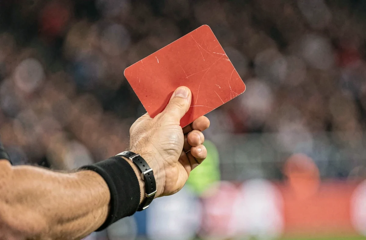 Gros plan sur la main d'un arbitre brandissant un carton rouge lors d'un match de football, foule floue en arrière-plan