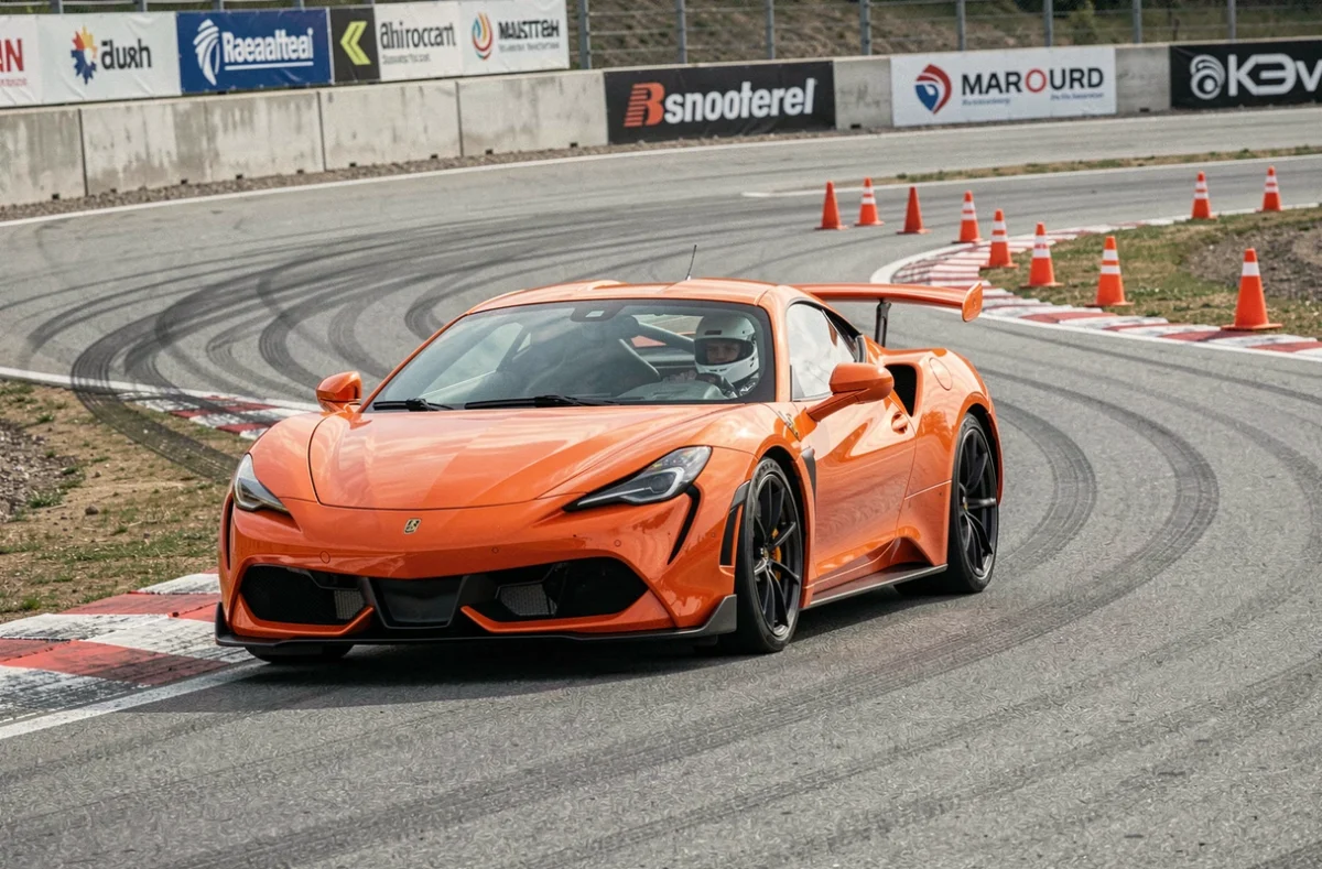Voiture de sport orange en pleine courbe sur un circuit lors d'un stage de pilotage, avec traces de pneus sur l'asphalte